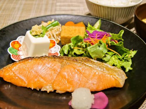 um prato preto com um pedaço de peixe e uma salada em APA Hotel Asakusa Kaminarimon em Tóquio