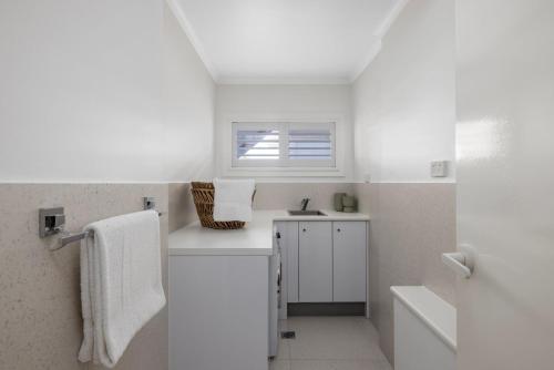 une salle de bain blanche avec un lavabo et une fenêtre dans l'établissement Waves at Boat Harbour, 65 Kingsley Dr - stunning house, fantastic waterviews and dog friendly, à Boat Harbour