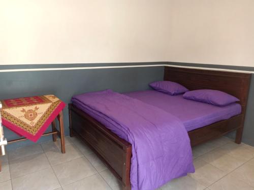 a bed with purple sheets and a table in a room at Homestay Anggun Bromo in Bromo