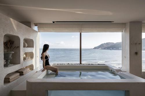 a woman sitting in a bath tub looking out at the ocean at HoHo House Songjeong in Busan