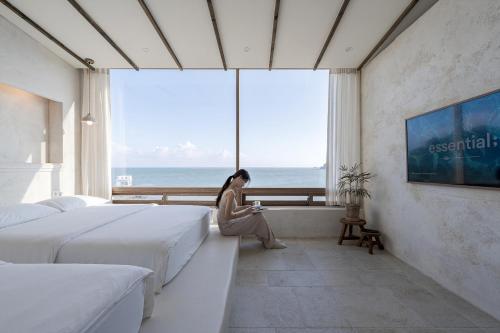 a woman sitting in a hotel room looking out the window at HoHo House Songjeong in Busan