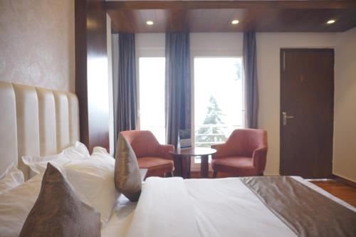 a hotel room with a bed and two chairs at Sangam by Stotrak, Jhula Ghar Mussoorie in Mussoorie