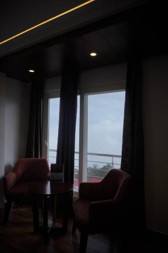 a living room with two chairs and a table and a window at Sangam by Stotrak, Jhula Ghar Mussoorie in Mussoorie
