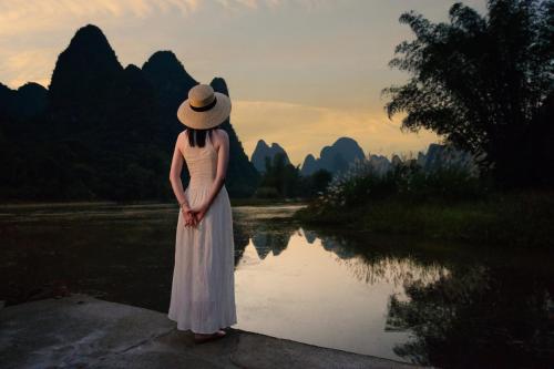 a woman in a hat standing in front of a river at The Apsara Lodge-Airport or TS Free pick-up over 3 nights in Yangshuo