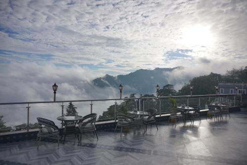 a balcony with tables and chairs and a view of the mountains at Sangam by Stotrak, Jhula Ghar Mussoorie in Mussoorie