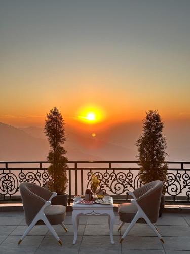 a sunset on a balcony with chairs and a table at Royalpine Rosastays Kasauli in Kasauli