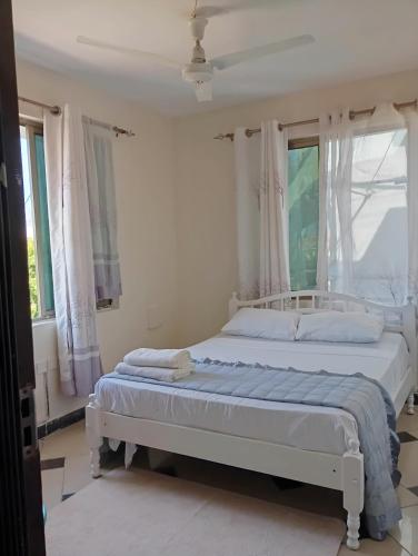 a white bedroom with two beds and windows at G-wel's Sun Sweet Apartment in Mombasa