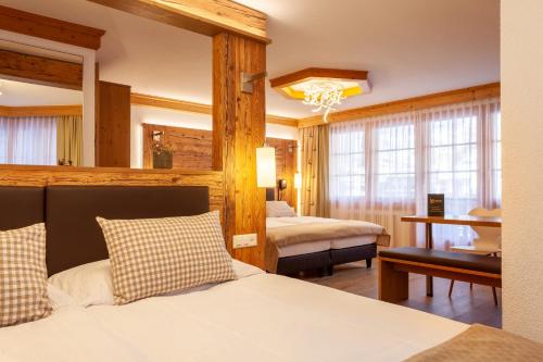 a hotel room with two beds and a desk at Hotel Jägerhof in Zermatt