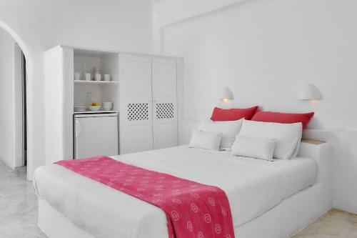 a white bedroom with a large white bed with red pillows at Finikia Memories Hotel in Oia