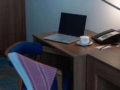 a desk with a laptop and a phone and a cup of coffee at Novotel Jazan in Jazan