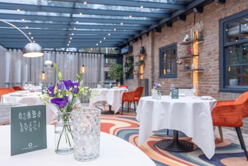 a dining room with white tables and chairs and flowers at Fletcher Hotel-Restaurant Klein Zwitserland in Heelsum