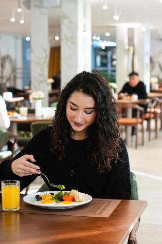 a woman sitting at a table with a plate of food at Almaty Hotel in Almaty