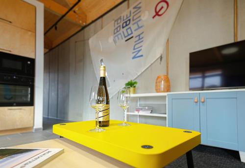 a yellow table with a bottle and two glasses on it at Kalóz apartmanház Velence in Velence