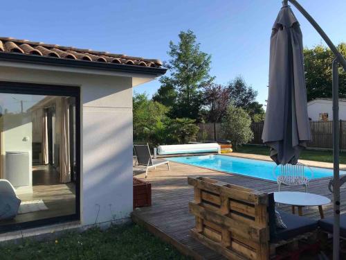 - une terrasse avec un parasol à côté de la piscine dans l'établissement Guest House avec piscine et jardin Privatifs, à Le Pian-Médoc