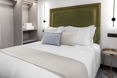 a white bed with white pillows and a green headboard at Hotel Aptos Alejandra Home by Maxi Hoteles in Granada