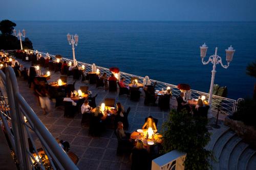 a group of people sitting at tables on a balcony with the ocean at Hotel Kalura in Cefalù