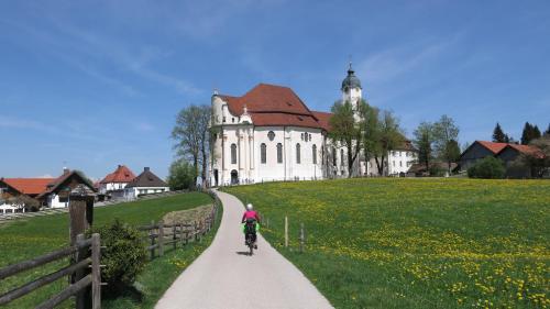 a person riding a bike down a path in front of a building at Apparthotel - Pension Ammertaler Hof in Saulgrub