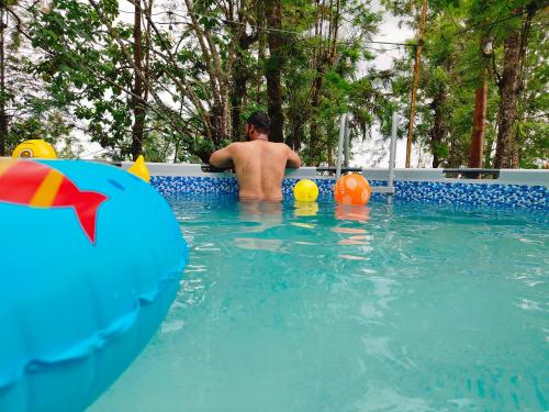 a man sitting in a swimming pool with an inflatable at Cicadas Nature Resort - A Frame cottages in Wayanad