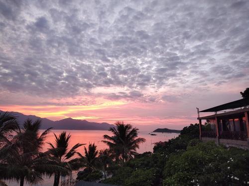 a sunset over the ocean with palm trees and a building at Green Oasis Nha Trang Resort in Nha Trang
