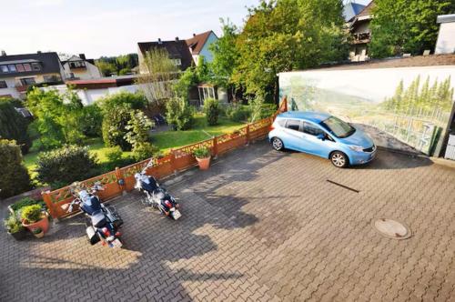 a blue car and two motorcycles parked in a parking lot at HIRSCH FeWo Burgberg - Parkplatz - Zentral in Bad Harzburg