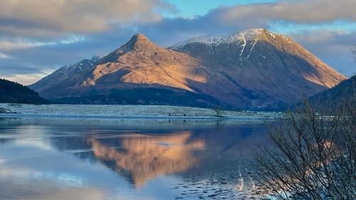 a mountain reflecting in a body of water at The Heronry Hideaway with luxury hot tub in Ballachulish