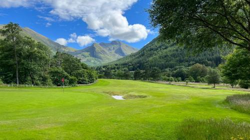 a green golf course with mountains in the background at The Heronry Hideaway with luxury hot tub in Ballachulish