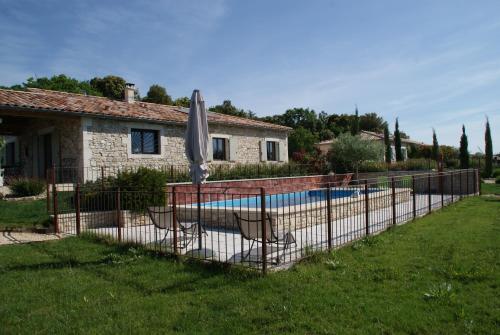 une clôture avec un parasol et des chaises à côté d'une piscine dans l'établissement GRAIN de SOLEIL, à Orgnac-lʼAven
