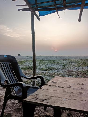 a table and a chair sitting on a beach with the sunset at Beach Clan Dorms in Alleppey