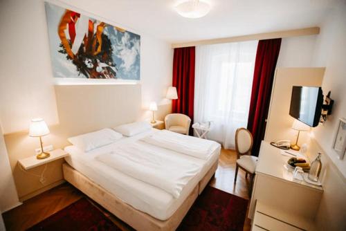 a bedroom with a large white bed and a tv at Boutique Hotel Goldenes Lamm Villach in Villach