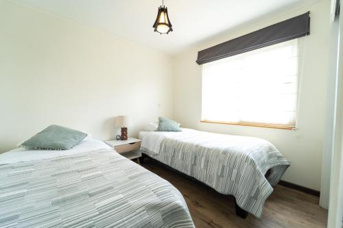 two beds in a white room with a window at Departamentos Nómades del Lago in Puerto Varas