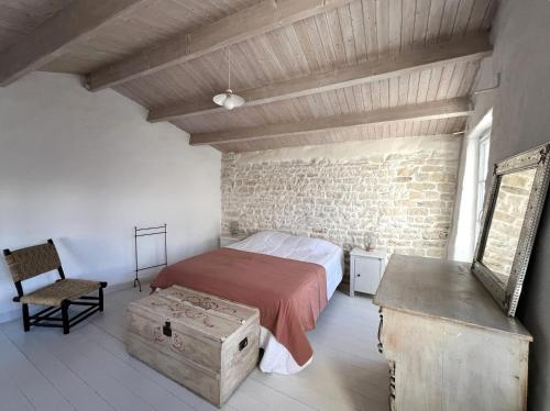 ein Schlafzimmer mit einem Bett, einem Stuhl und einer Ziegelwand in der Unterkunft Maison LA BEURELIÈRE proche Plage in Sainte-Marie-de-Ré