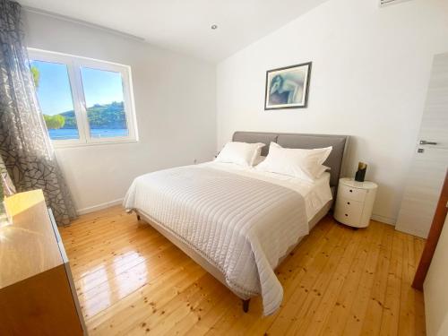 a bedroom with a bed with white sheets and a window at Villa Moro: Beachfront Privacy in Trstenik