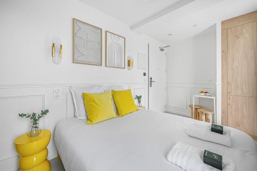 a white bedroom with a large bed with yellow pillows at JIJI Suites in Combs-la-Ville
