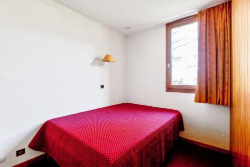 Ce lit rouge se trouve dans une chambre blanche dotée d'une fenêtre. dans l'établissement Résidence Le Hameau du Sauget - maeva Home - 2 Pièces 4 Personnes Confort MAE-8461, à La Plagne Tarentaise