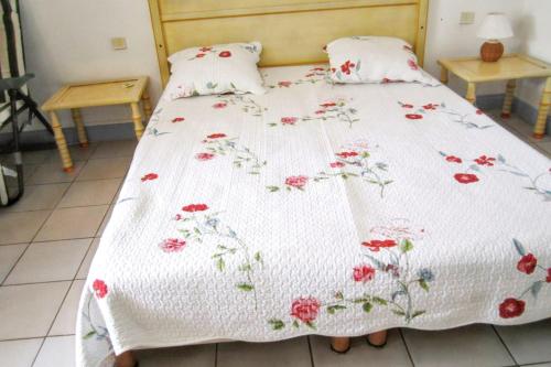 a bed with a white blanket with red flowers on it at Studio charmant à Sainte Anne avec terrasse - 26 m² in Sainte-Anne