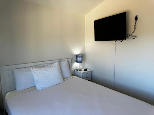 a bedroom with a white bed with a television on the wall at Westport Inn Cabins in Westport