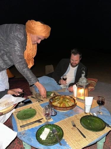 a group of people sitting around a table with plates of food at Camp Mbark authentic in Mhamid