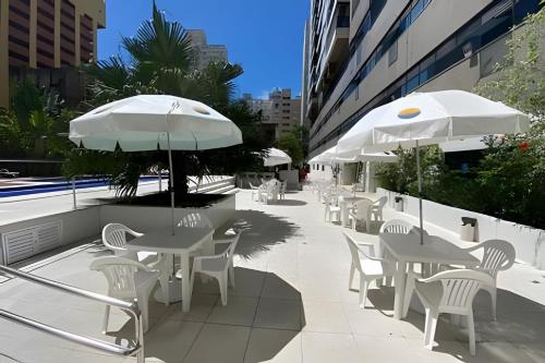 a patio with white tables and chairs and umbrellas at Paraíso com piscina: Pitangueiras Lazer Completo in Guarujá