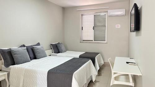 two beds in a white room with a window at Hotel Atlântico in Americana