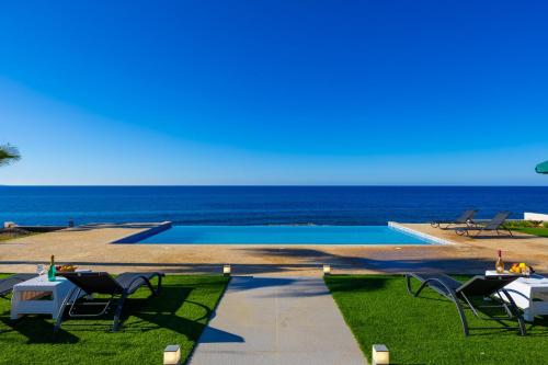 a pool with chairs and a table and the ocean at Villa Stella Sunset in Nea Dimmata