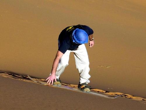 a man standing on a snowboard on the ground at Camel Luxury Camp in Merzouga
