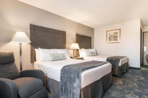 a hotel room with two beds and a chair at American Inn & Suites Metro Airport in Romulus