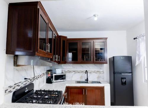 a kitchen with wooden cabinets and a black refrigerator at Villas Hillside apt 3 in Santa Bárbara de Samaná