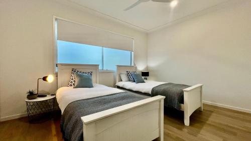 two beds in a room with a large window at Coastal Escape Watch Horses Pass Walk to Beach in Redcliffe