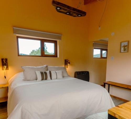 een slaapkamer met een groot wit bed met twee ramen bij Berberis Apart in El Chalten