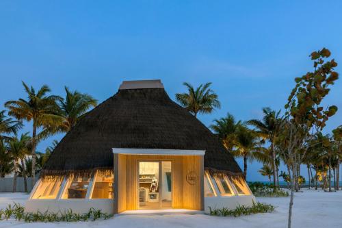 a thatched hut on the beach with palm trees at Centara Mirage Lagoon Maldives in Nakachchafushi