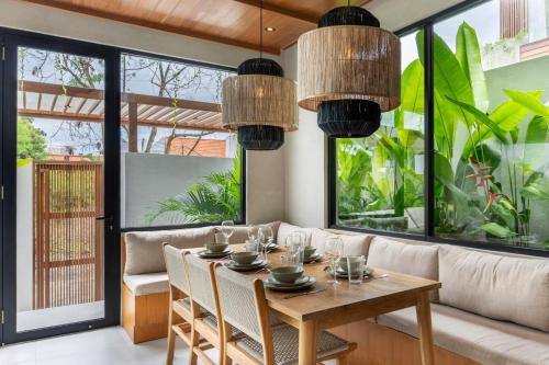 a dining room with a table and chairs and large windows at Nanna Villa Unit 2 by Betterplace in Tumbak Bayuh