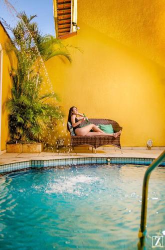 a woman sitting in a chair next to a swimming pool at Pousada Vale Valparaíso Inn- Polo gastronômico in Petrópolis