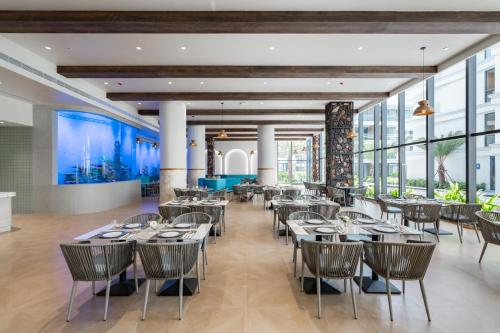 a dining room with tables and chairs and large windows at Kora Beach Resort Phuket in Bang Tao Beach