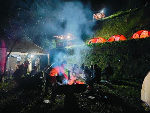a group of people sitting around a campfire at night at D'Sentra Camping Ground in Pengalengan